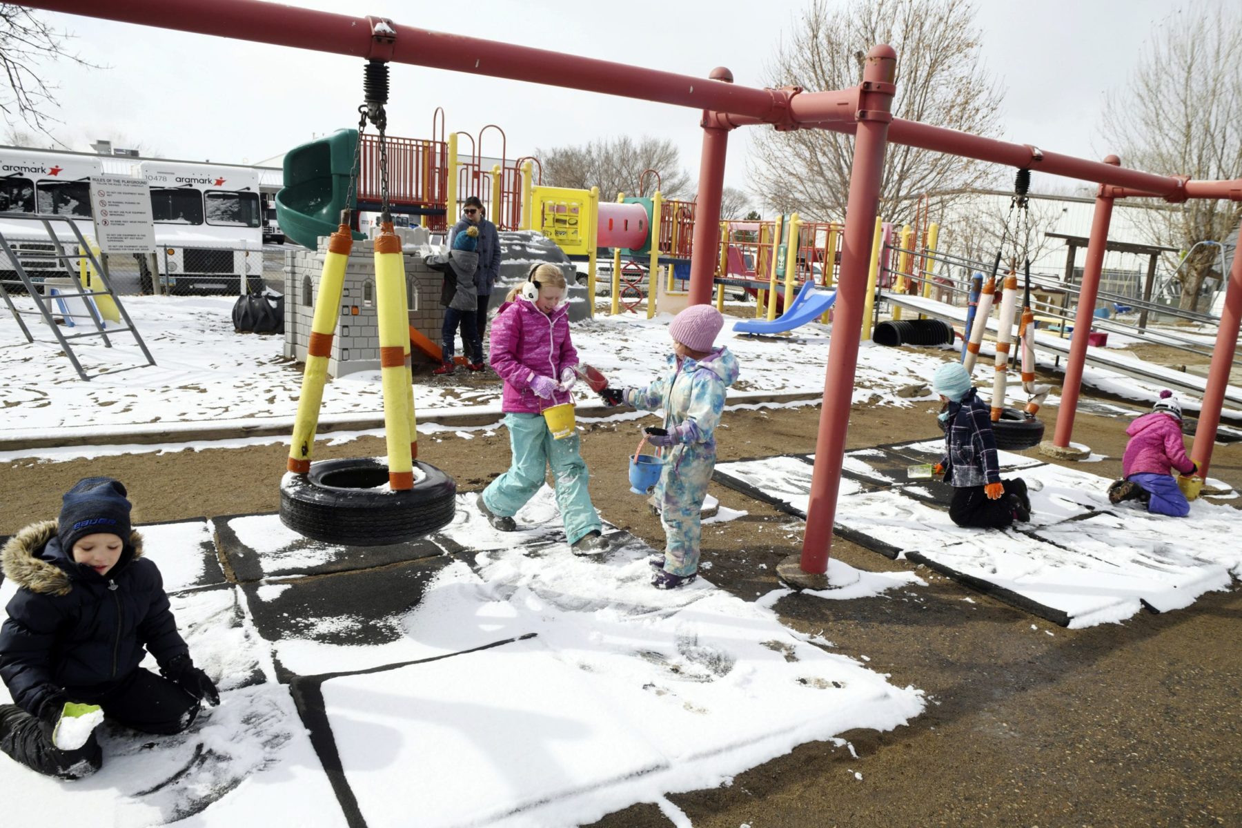 Children playing on a swing set with snow on the ground.