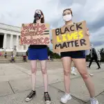 Two women stand with anti-racist signs.