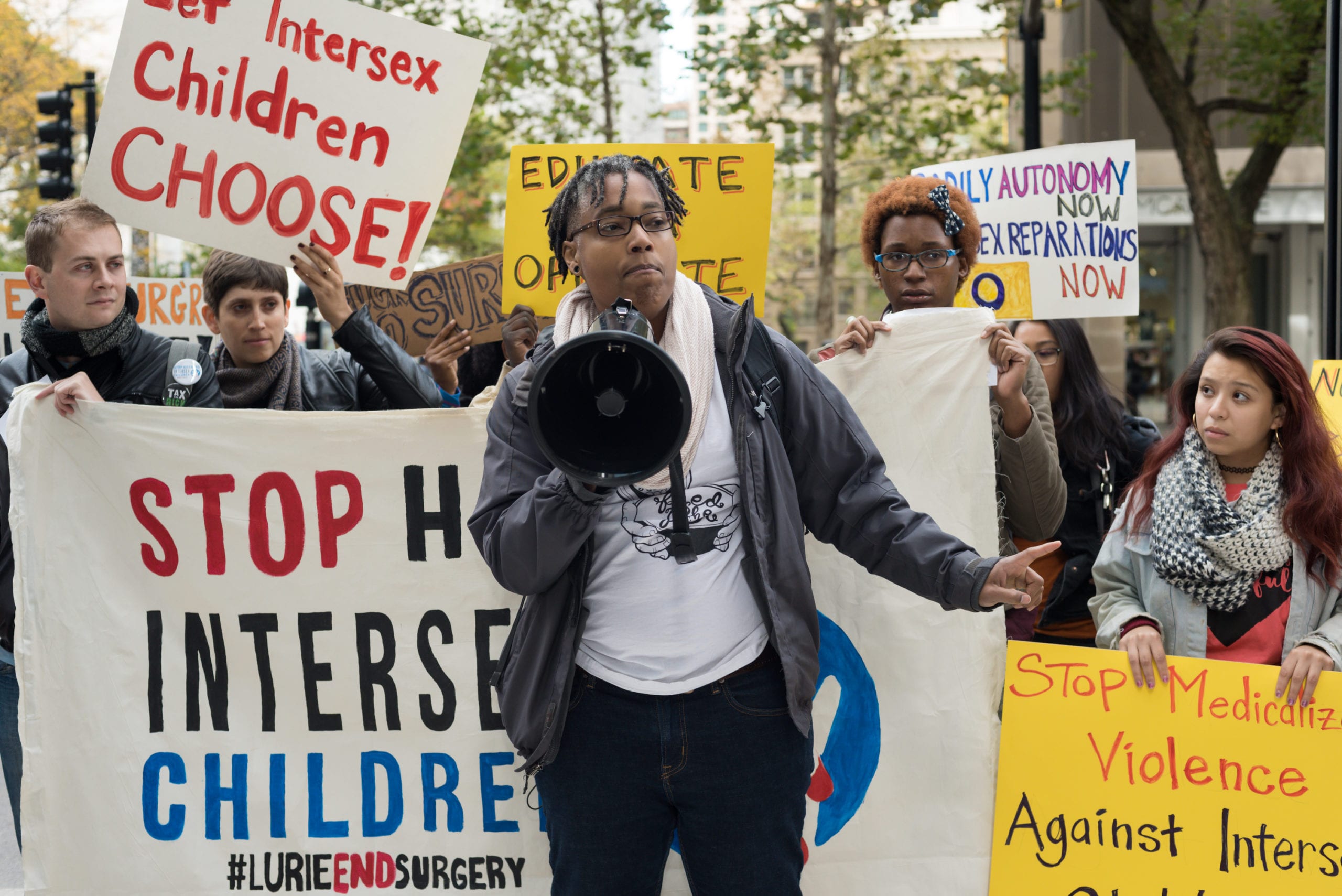 A person stands with a megaphone at a protest against intersex surgeries.