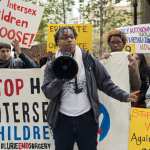 A person stands with a megaphone at a protest against intersex surgeries.