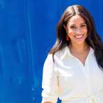 Meghan Markle smiles at camera against a blue background.