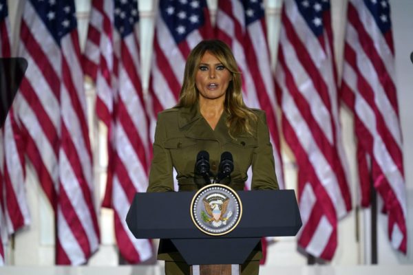 Melania Trump standing in front of a row of American flags.