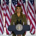 Melania Trump standing in front of a row of American flags.