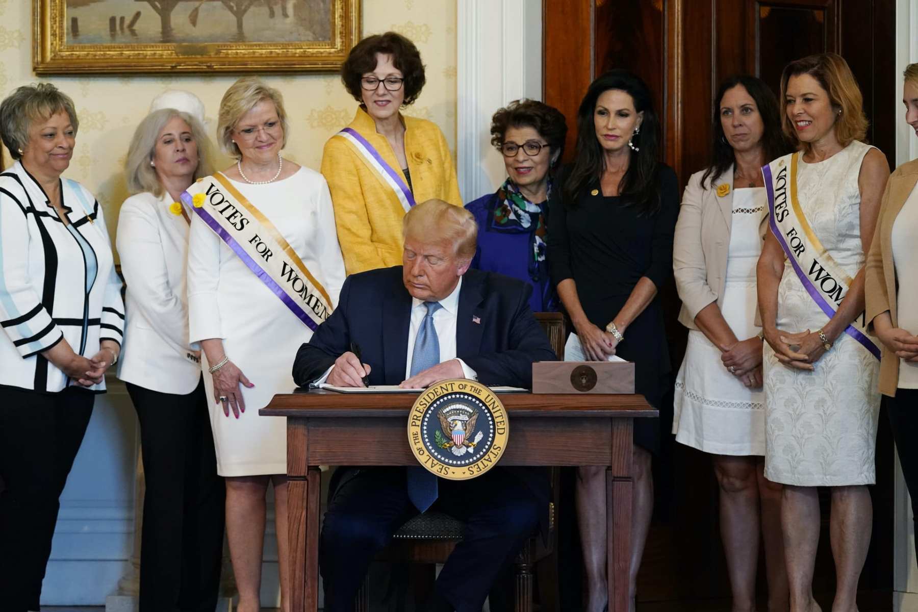 President Donald Trump signs a document surrounded by women surrogates.