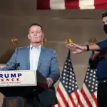 Richard Grenell stands at a Trump-Pence podium.
