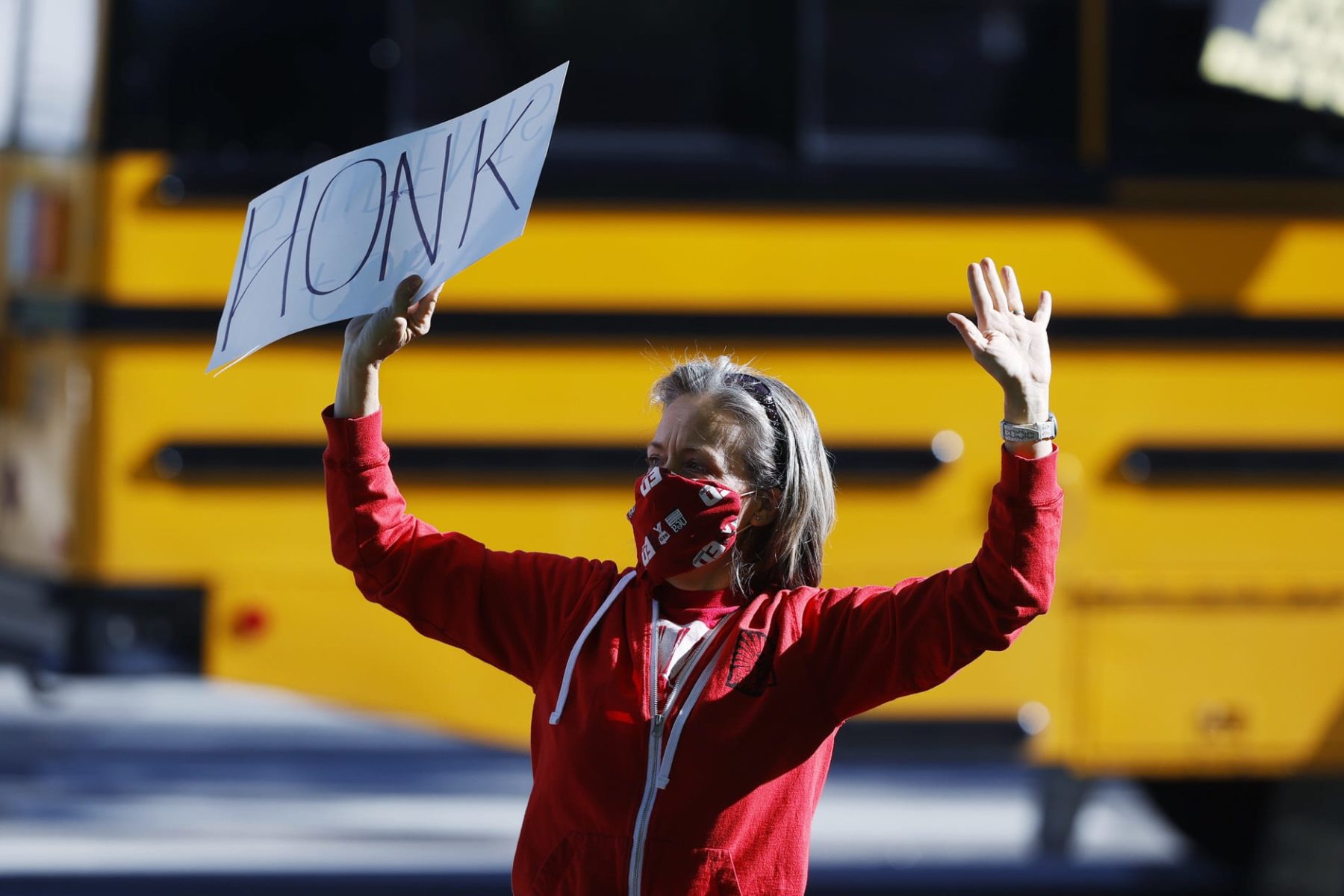 Lara Center, dressed in a red hoodie and holding a sign that says HONK in all caps above her head, protests in Denver to protect public schools from budget cuts.