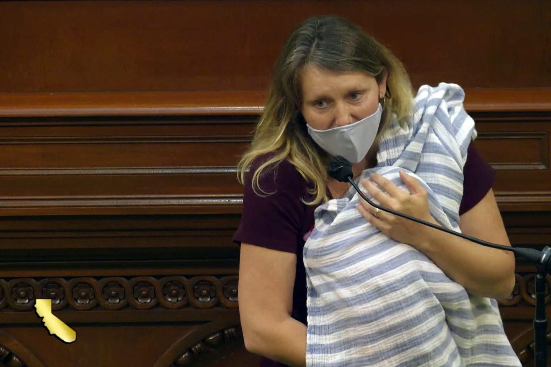 California Assemblymember Buffy Wicks holds her newborn while speaking into a microphone.