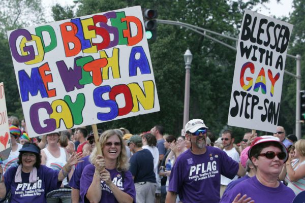 A group of people march with signs supporting their LGBTQ+ children.