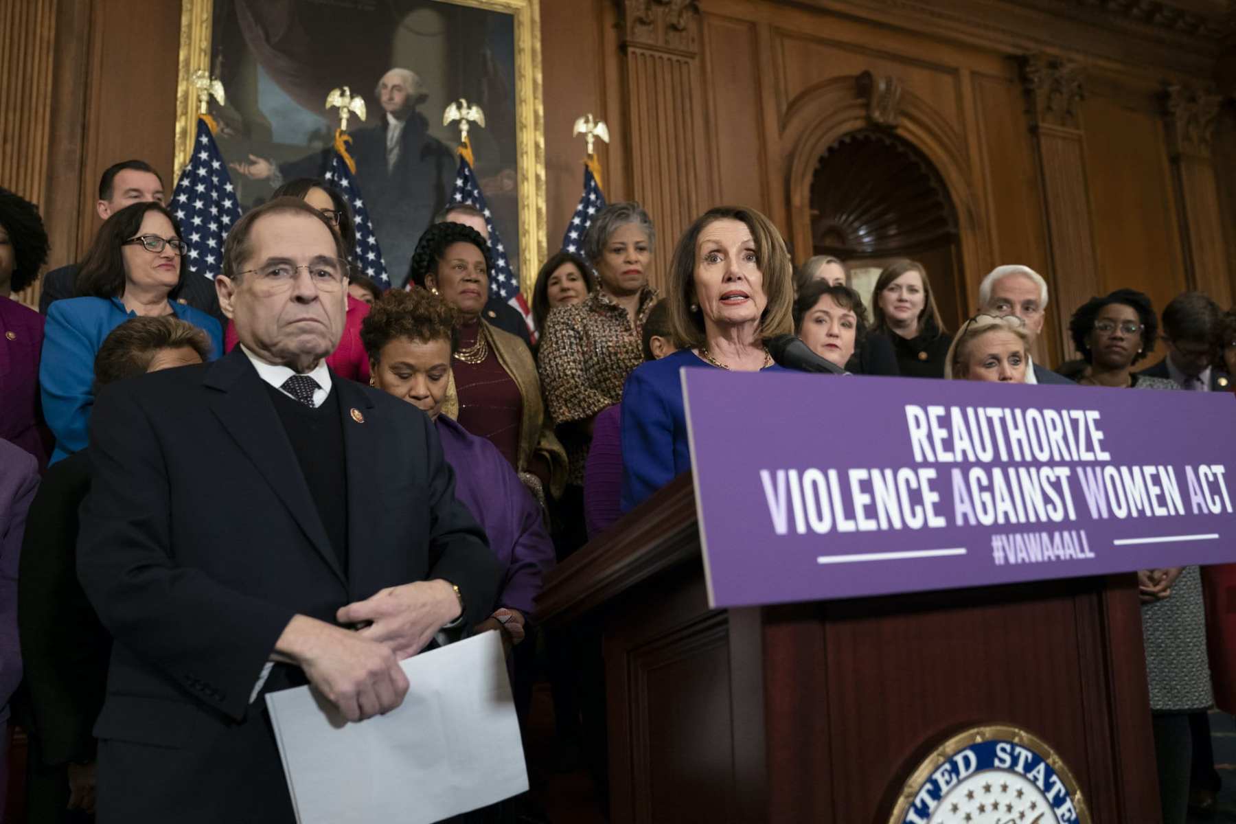 Nancy Pelosi and other legislators stand at a podium that reads "Reauthorize Violence Against Women Act"