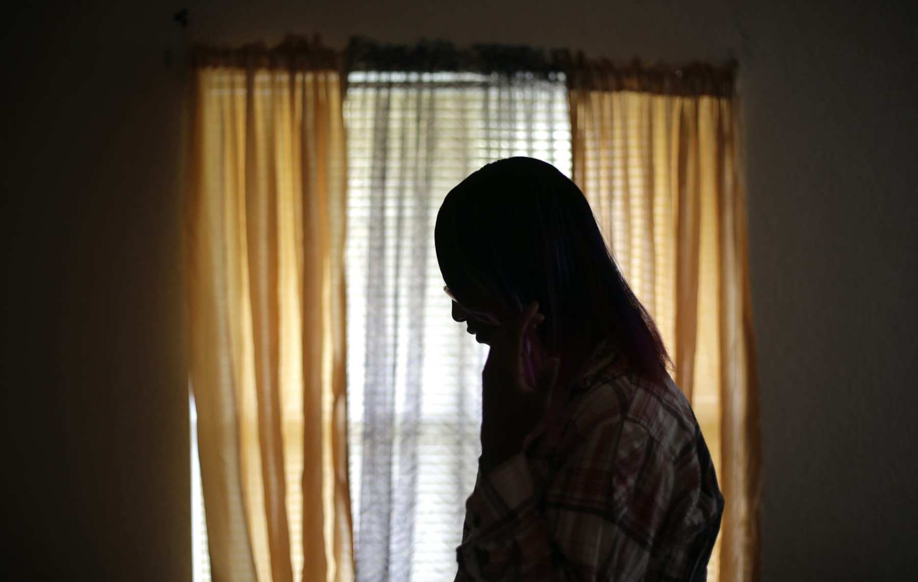 An outline of a transgender teen standing by the window. Her face is hidden.