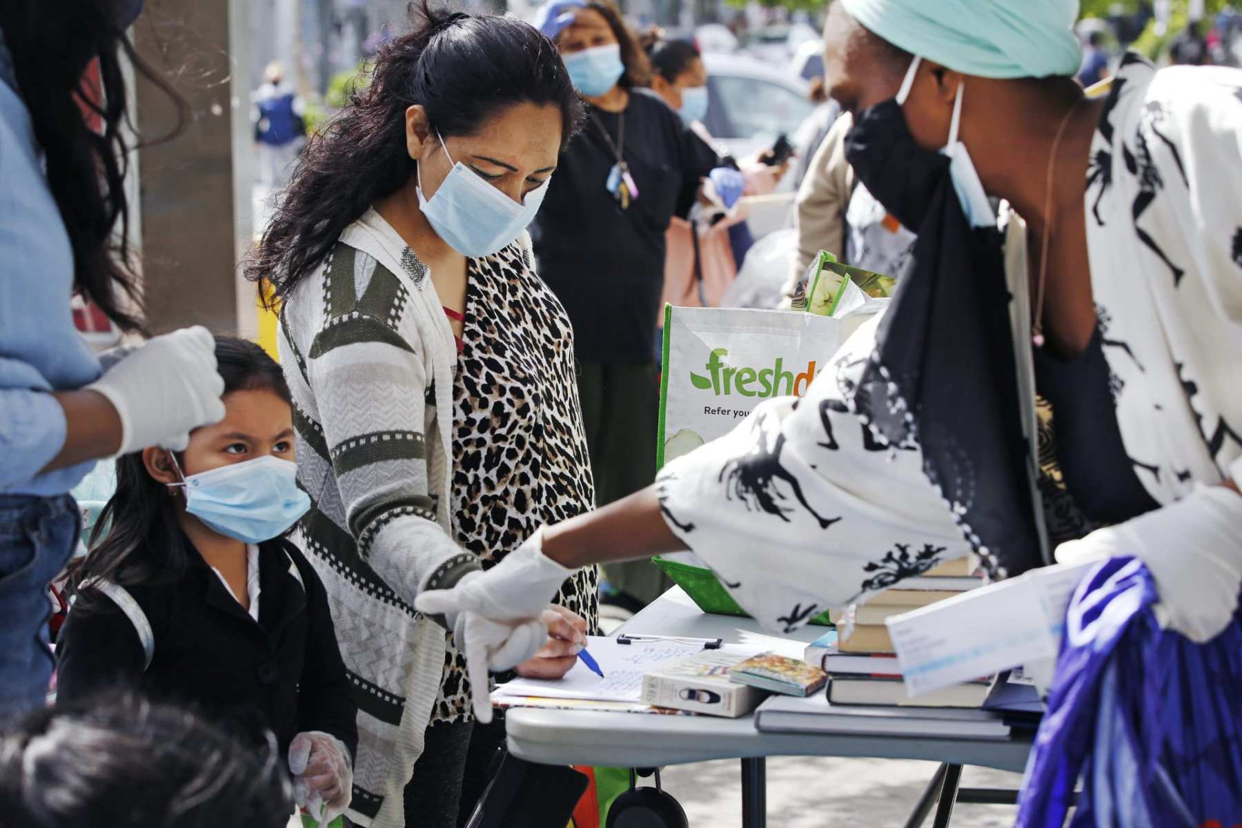 Volunteer Sequaña Williams-Hechavarria, right, instructs youngster Jade Suarez to look beneath the table for books as Jade's mother, Maria, signs up for assistance and free supplies provided by Sistas Van during the coronavirus outbreak at a busy Bushwick intersection in the Brooklyn borough of New York, Tuesday, May 19, 2020. Sistas Van was originally launched by the nonprofit Black Women's Blueprint to help survivors of sexual and reproductive violence and physical abuse. But during the coronavirus, the women's network has pivoted to delivering badly-needed resources to black and Hispanic communities, which have had some of the city's highest rates of contagion and death toll of the fast-spreading virus.