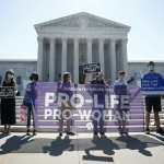 A group stands in front of the Supreme Court with a sign that reads, 