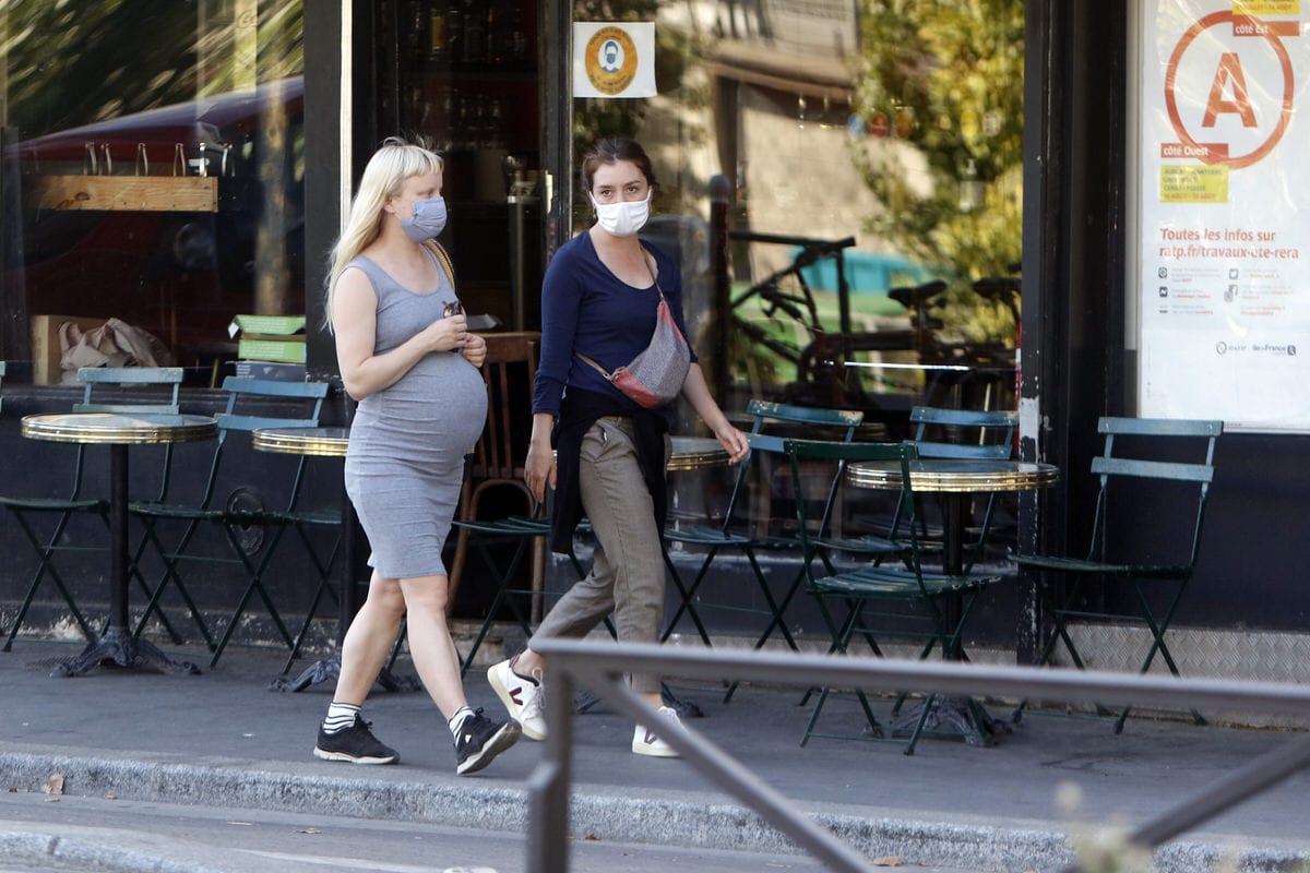 Two pregnant women wearing masks walk down the street.
