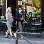 Two pregnant women wearing masks walk down the street.