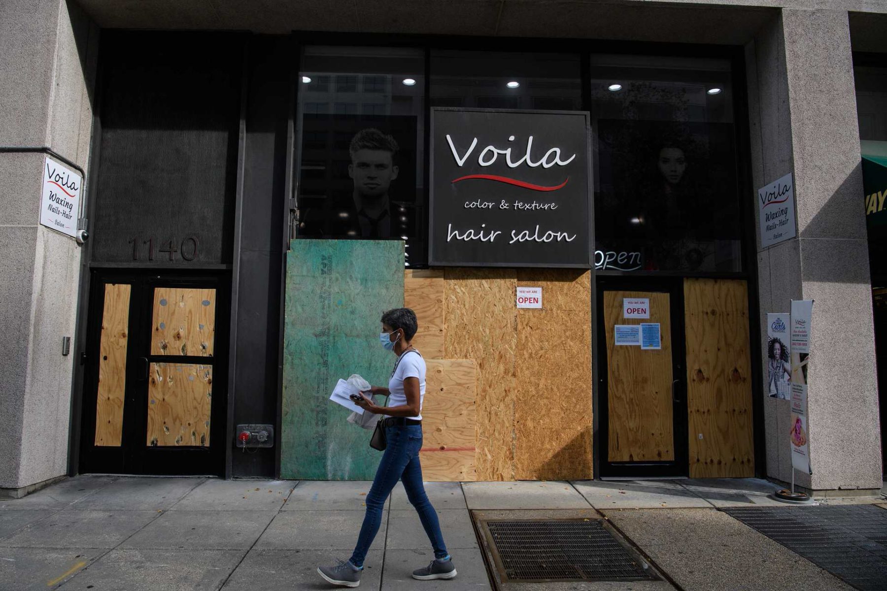 A woman walks by a boarded up business.