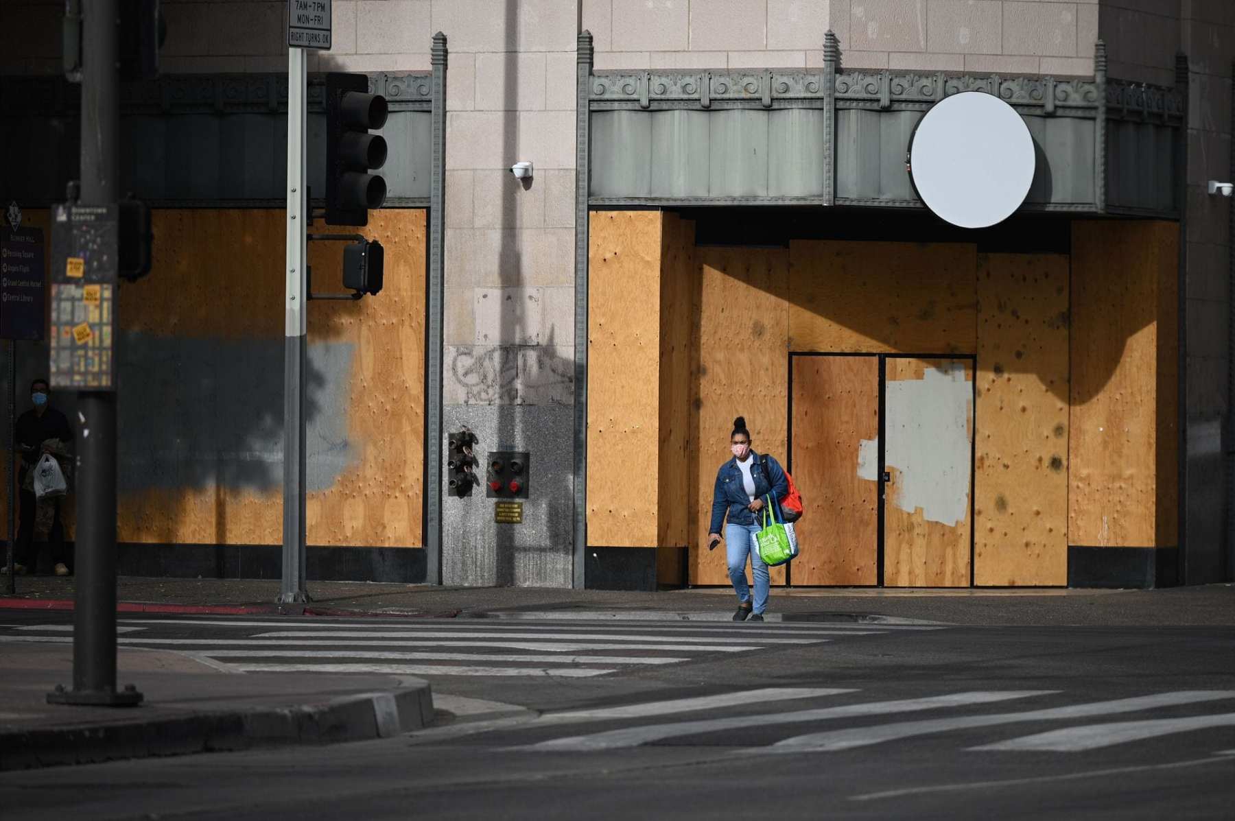 A woman wearing a facemask to prevent the spread of coronavirus walks past a boarded up storefront at the intersection of Hill Street and 5th Street in downtown Los Angeles, California, November 5, 2020 as the country awaits the result of the November 3 US presidential election. - Businesses in major US cities were boarded up in anticipation of unrest. The nail-biting US election was on the cusp of finally producing a winner Thursday, with Democrat Joe Biden declaring 