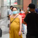 A pregnant woman wearing a face mask walks down the street.