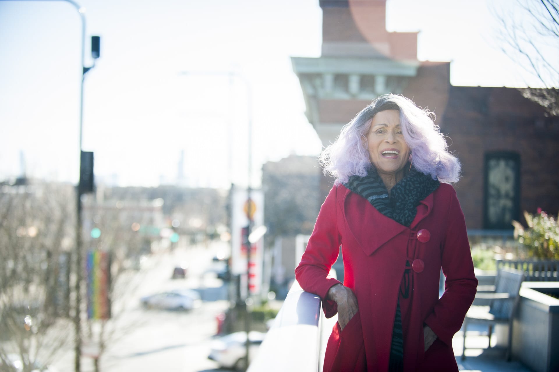 Gloria Allen stands on the terrace of her apartment building in a red coat.