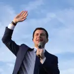 Pete Buttigieg waves while holding a microphone.