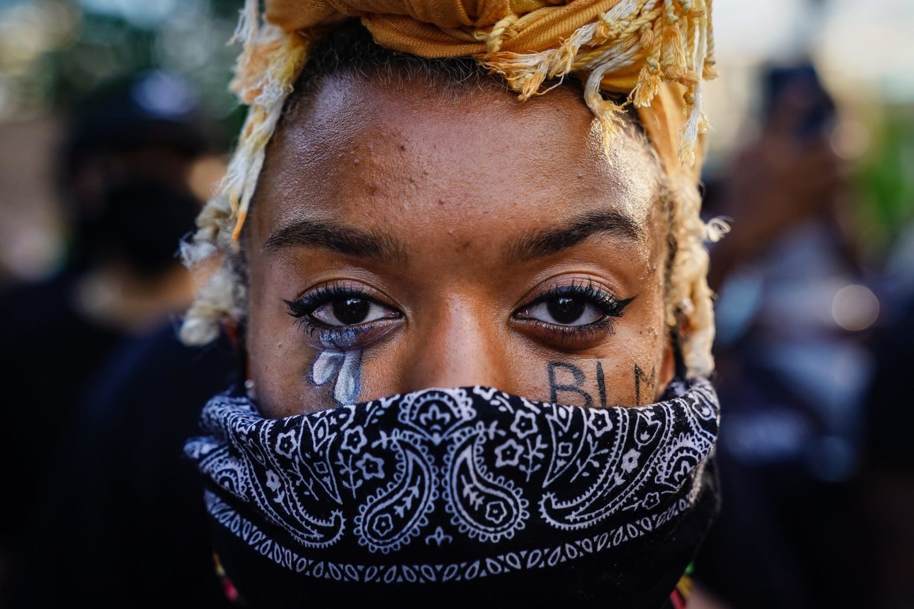 A woman wearing a bandana with BLM painted on her cheeks.