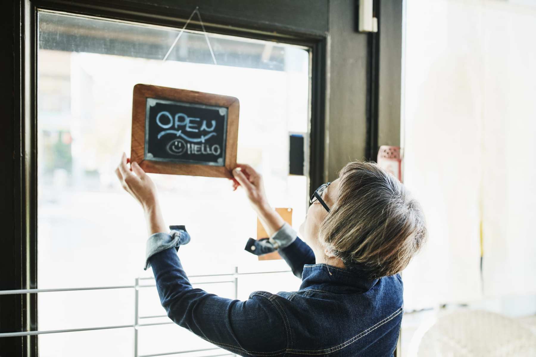 Senior female business owner turning open sign on door before opening boutique