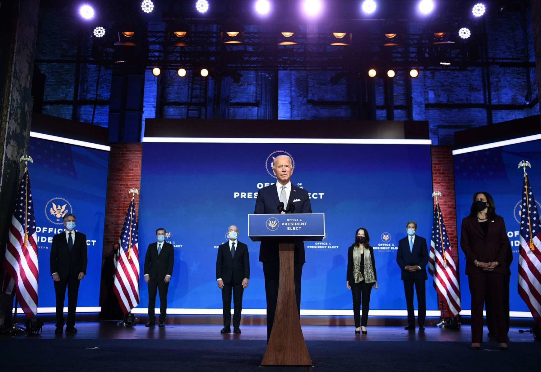 Biden standing at a podium surrounded by members of his Cabinet.