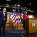 Nancy Pelosi stands at a podium with Chuck Schumer to her right.