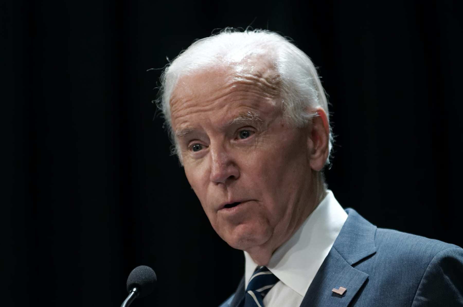 A close up photo of Joe Biden speaking into a microphone.
