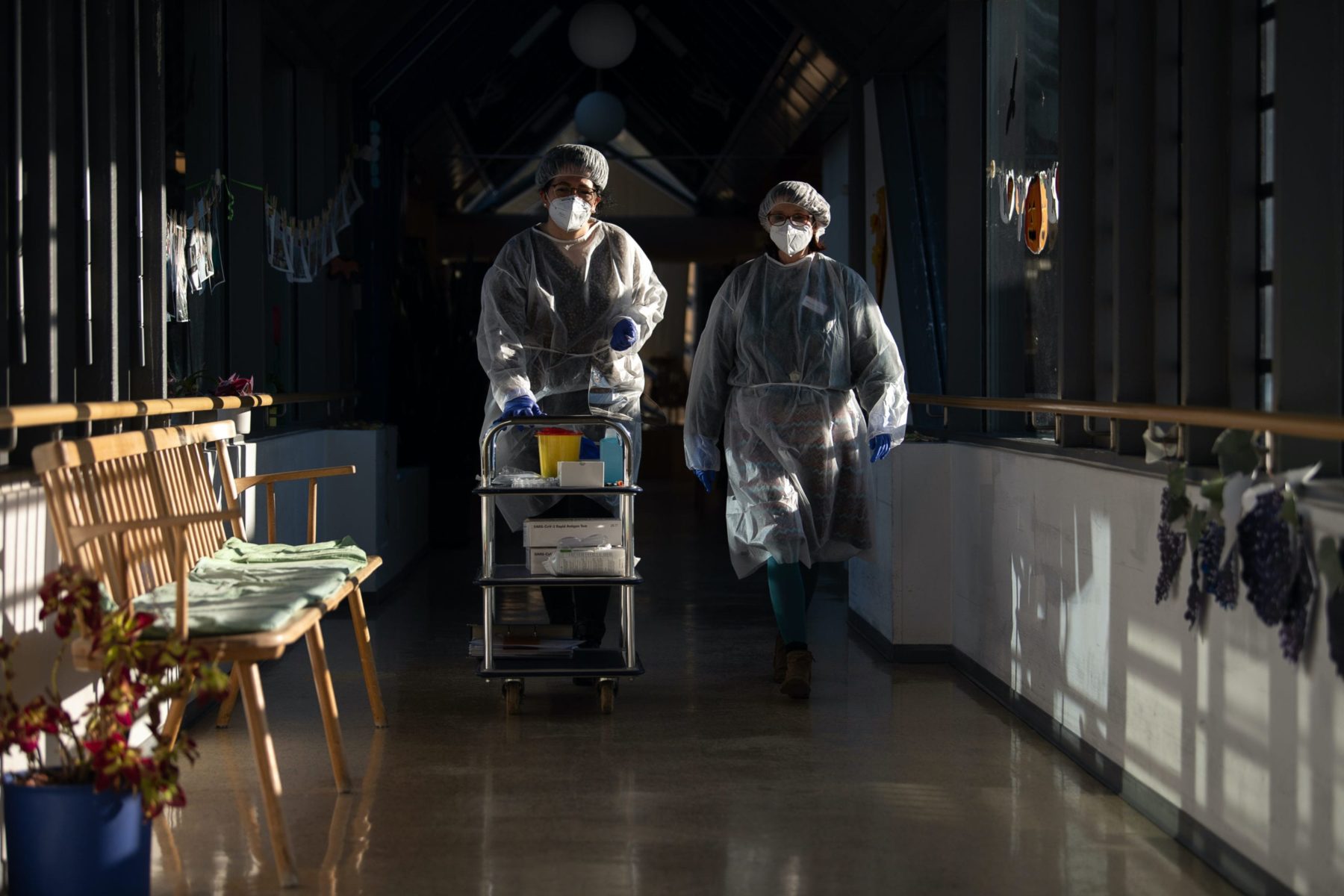 Two geriatric nurses walk through a corridor in the Pauline Krone Home for the Elderly of the Tübingen elderly care centre with protective equipment that they have put on to carry out rapid antigen-corona tests. (