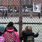 A group of children look at their school ground through a fence.