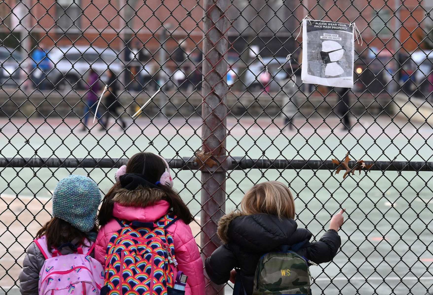 A group of children look at their school ground through a fence.