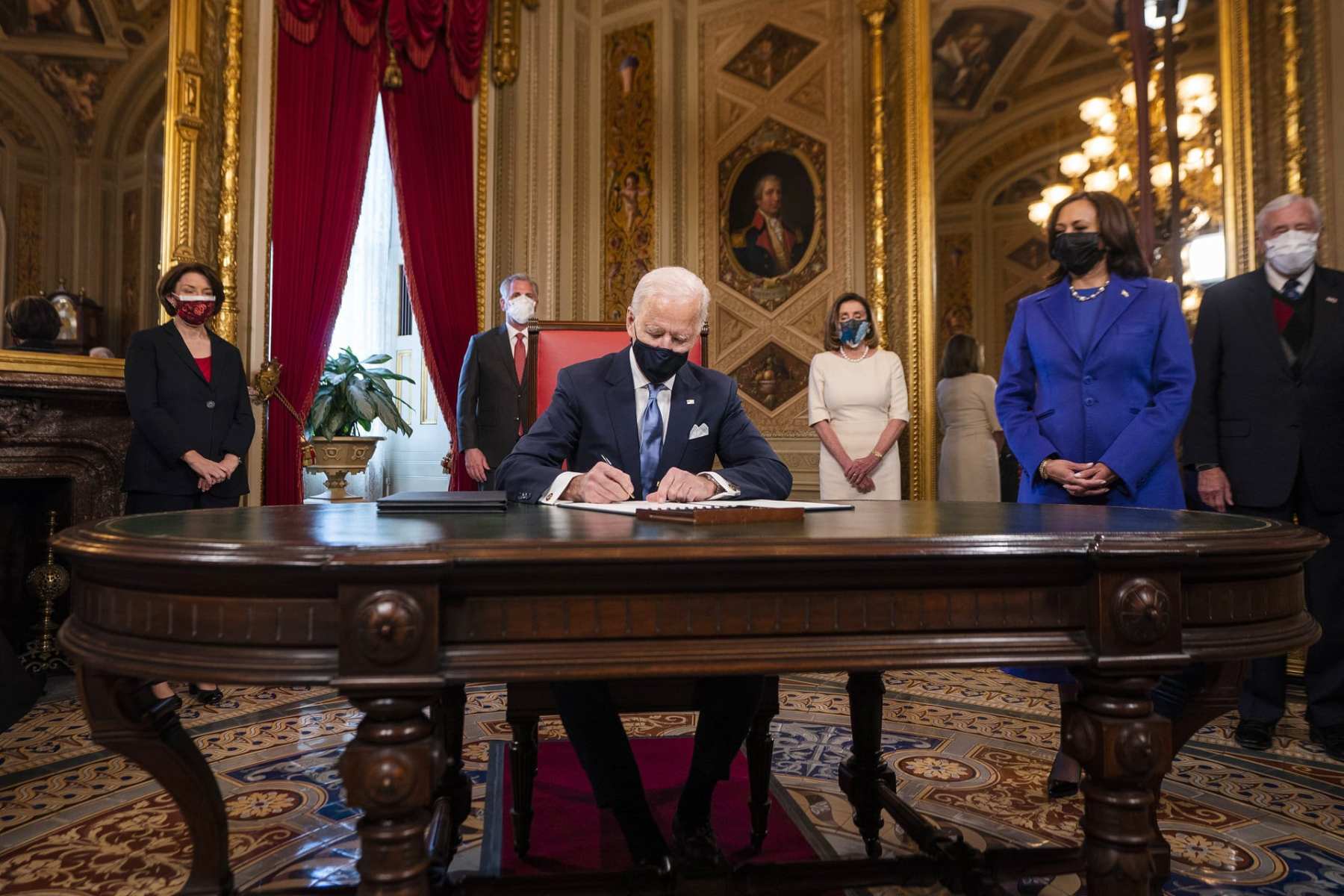 US President Joe Biden signs three documents at a table.