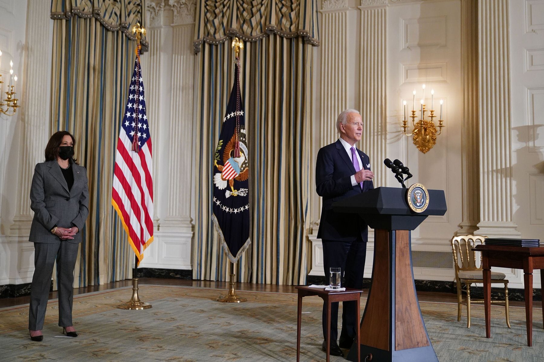 US Vice President Kamala Harris listens as US President Joe Biden speaks on racial equity at a podium in the White House state dining room.