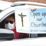 A demonstrators holding a sign out of a car window demanding restrictions that have closed churches be lifted.