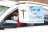 A demonstrators holding a sign out of a car window demanding restrictions that have closed churches be lifted.