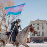 A person rides past the South Dakota Capitol with a trans flag.