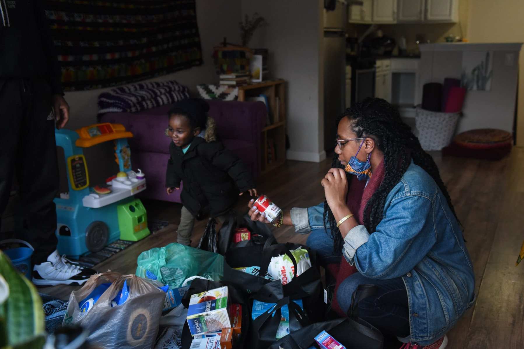 A woman looks at food and essential items as her child plays in the family room.
