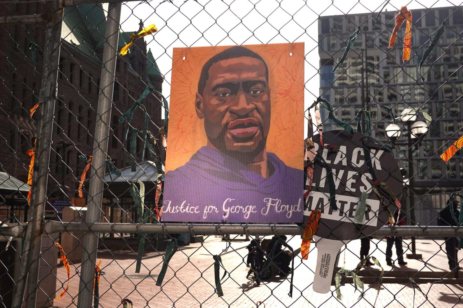 A illustration of George Floyd hangs on fencing next to a sign that reads 