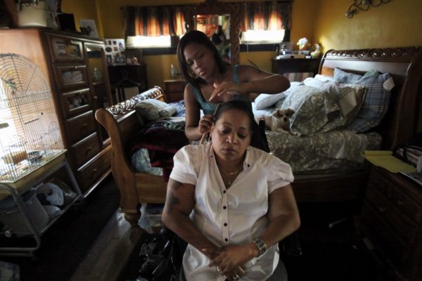 A home health aide brushes the hair of a patient in her home.