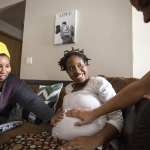 Two midwives tend an expectant mother on her couch.