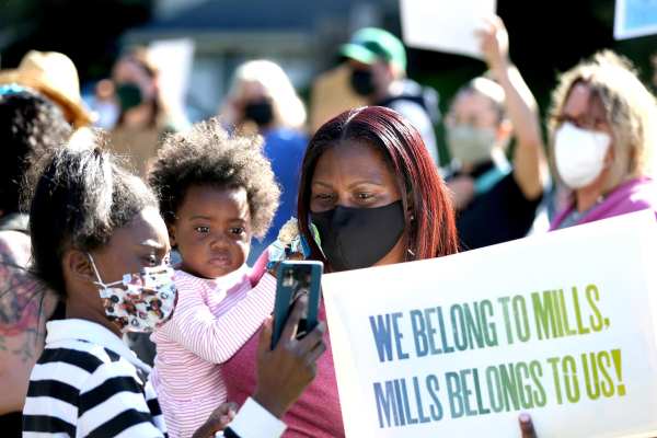 Skyler Mills, 10, left, Kinsey Mills, 2, and their mother Robin Mills, a Mills College alumna, hold up a sign during a rally at Mills College.