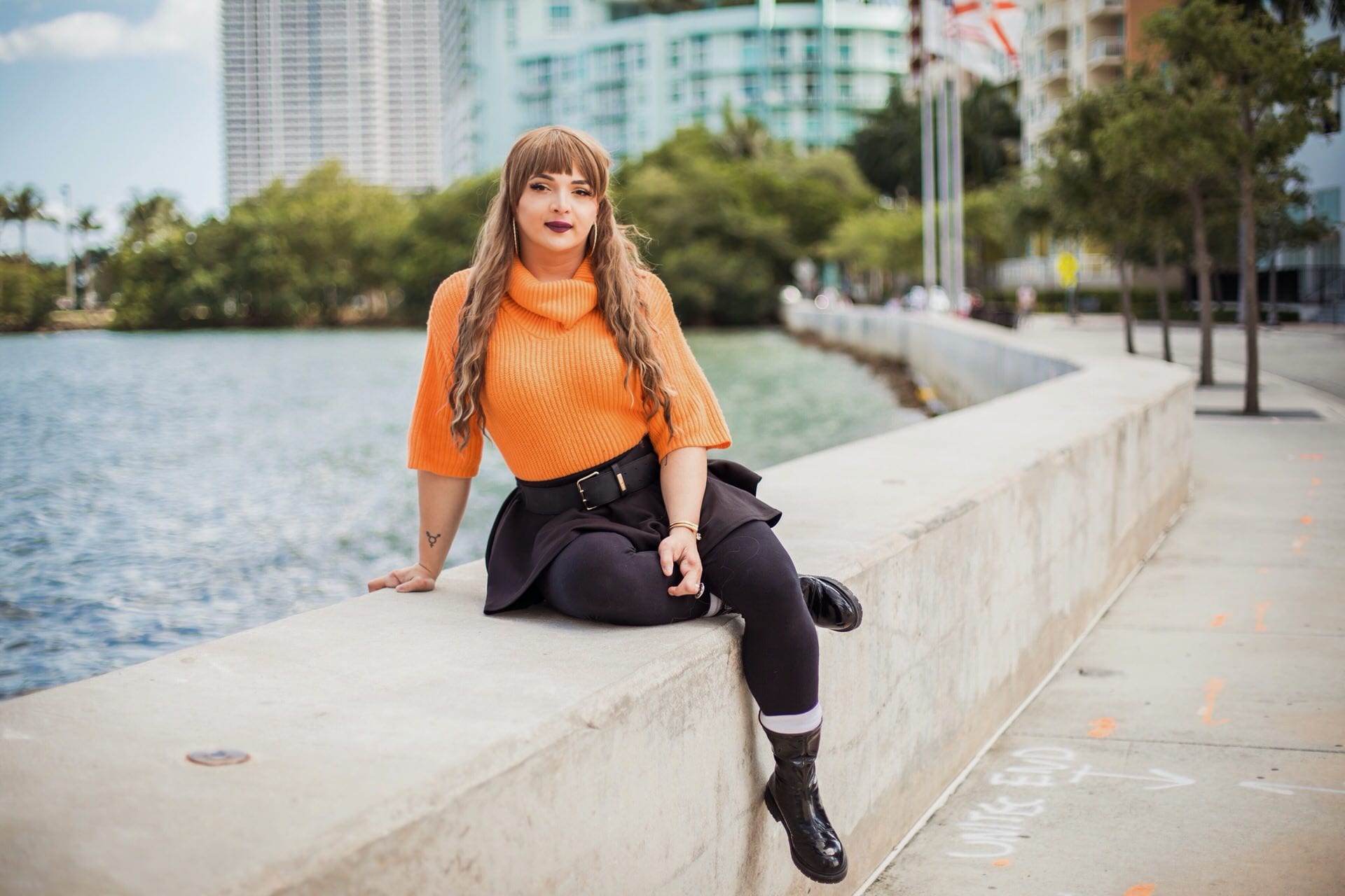 A woman sits on a retaining wall at a waterfront.