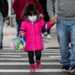 A small girl wearing a mask walks down the street in New York City.