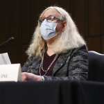 Dr. Rachel Levine speaking at a desk with a mask on.