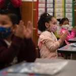 First graders wearing masks applaud in class