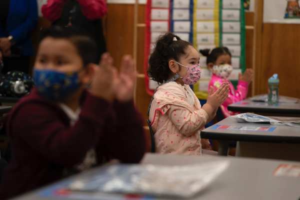 First graders wearing masks applaud in class