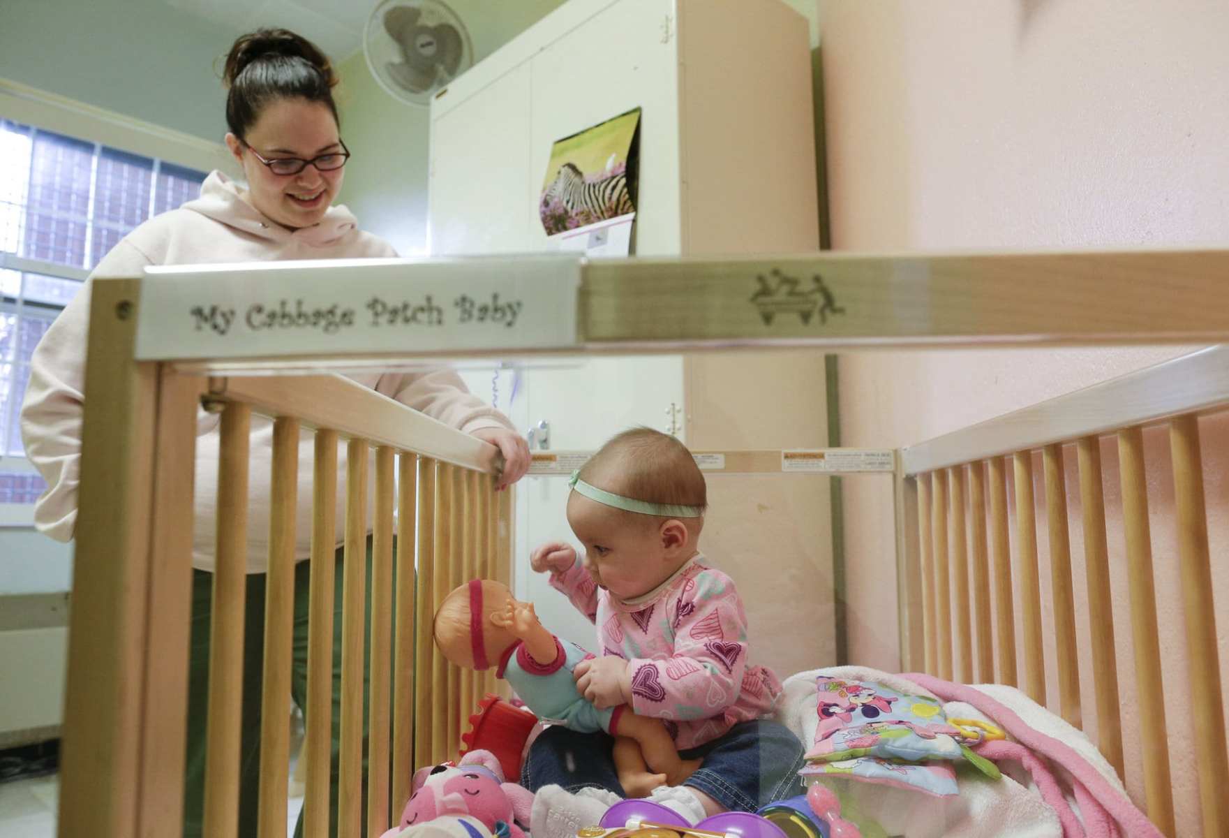 A mother watches over her daughter as she plays in her crib inside her room at a correctional facility.