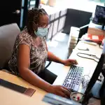 A Black women works behind a desk at an apartment building.