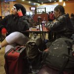 Queer youth sit with their belongings at a table in a fast food restaurant.