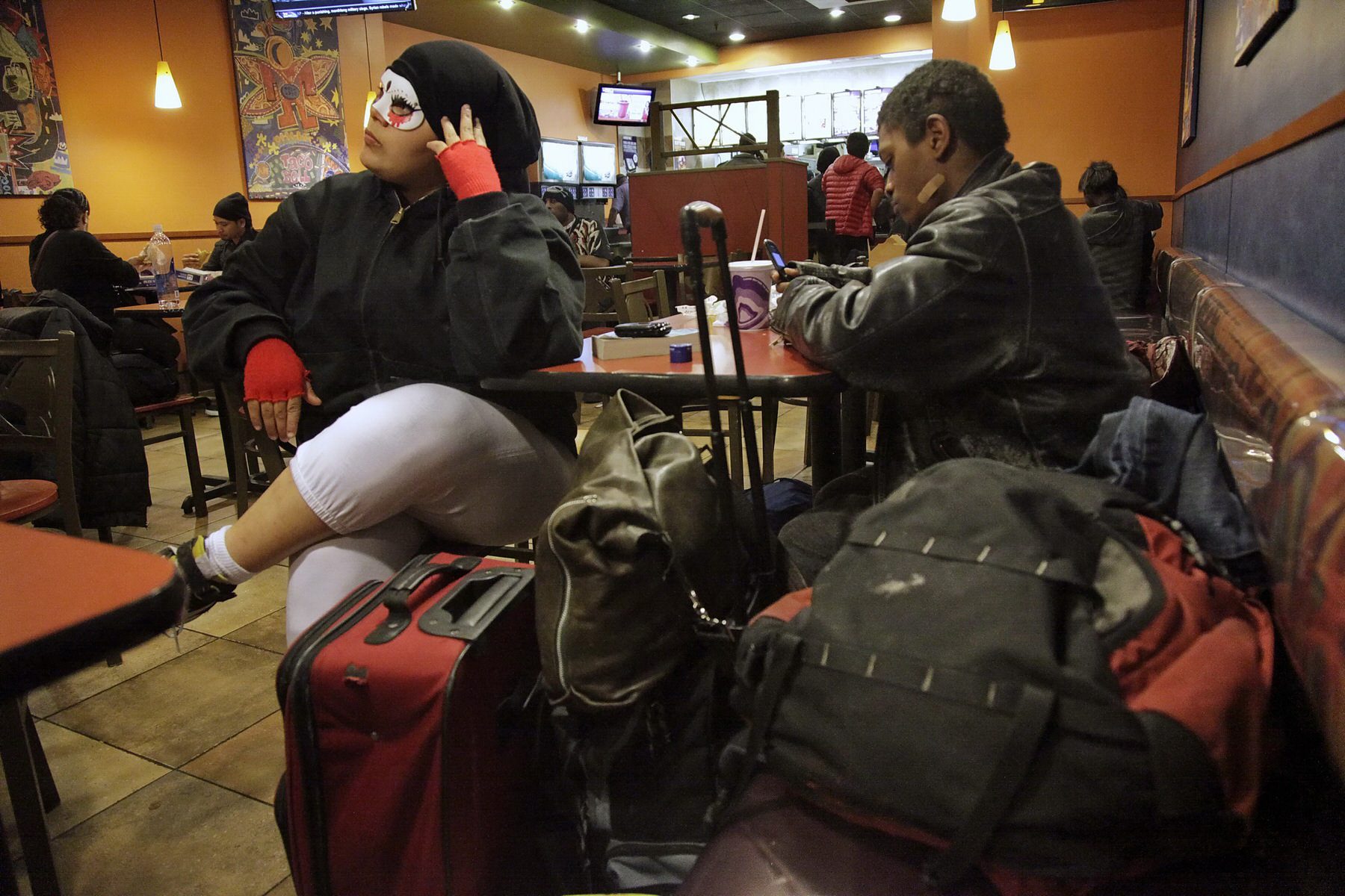 Queer youth sit with their belongings at a table in a fast food restaurant.
